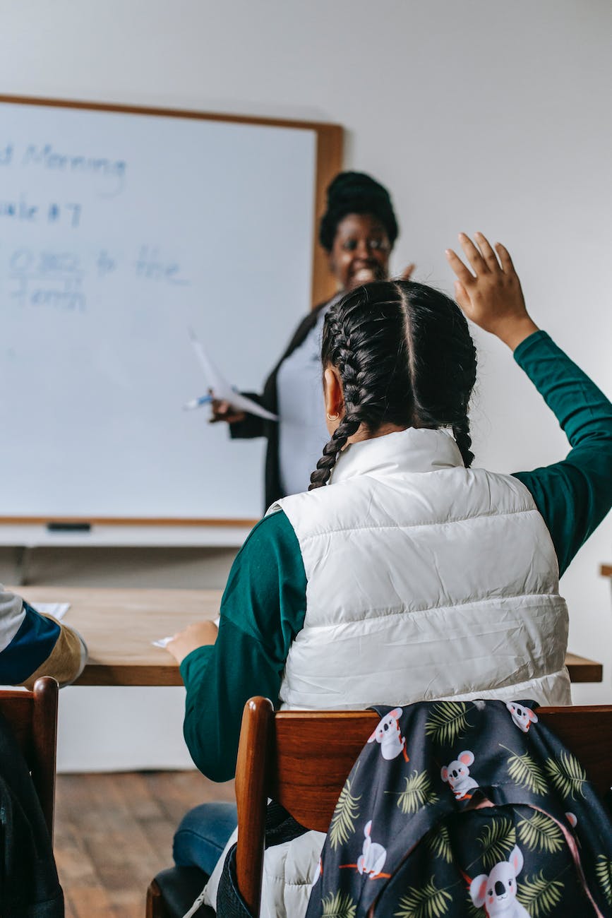 black female teacher looking at schoolgirl raising hand